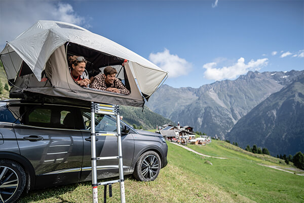 Couple looking out of their Yakima SkyRise Vehicle Roof Tent in the alps