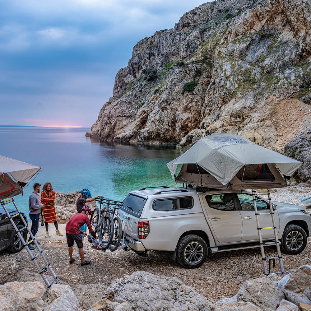 Two couples with roof tents on their vehicles parked in cove with sea back drop