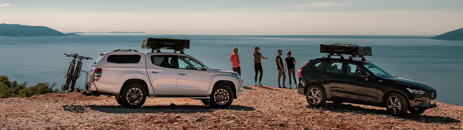 Two couples enjoy a sea view in fron of their cars with roof tents stowed away on the roof