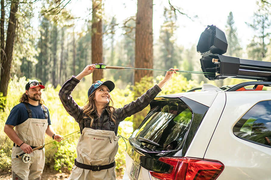 A woman loads a fishing into the Yakima DoubleHaul Fishing Rod Carrier on top of a white vehicle