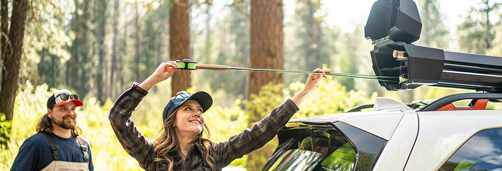 A woman loads a fishing into the Yakima DoubleHaul Fishing Rod Carrier on top of a white vehicle