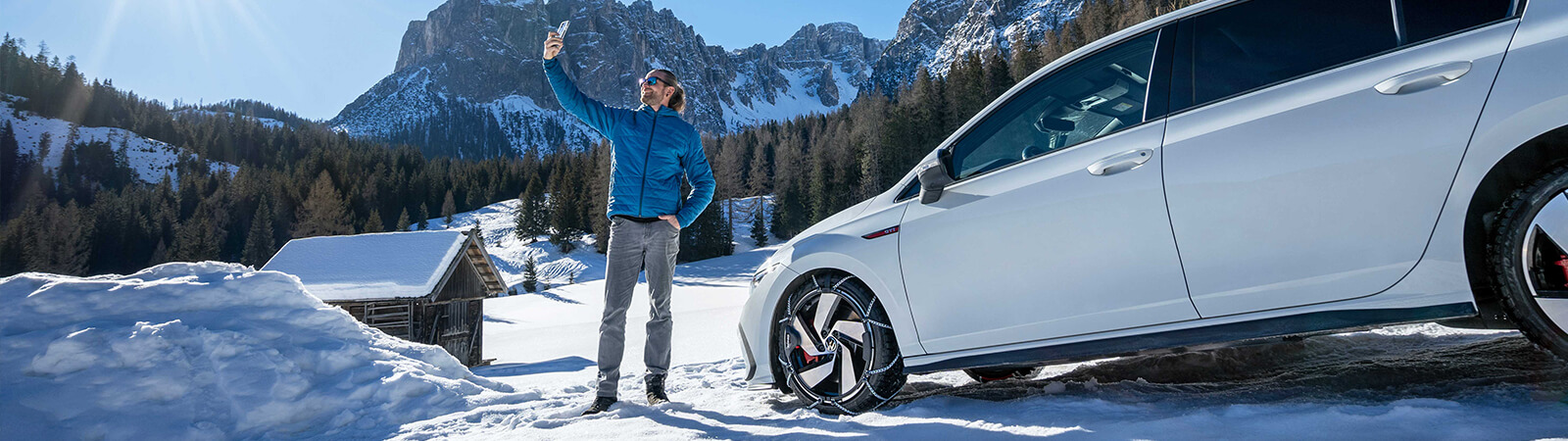 A man takes a 'selfie' in a mountain location with his car fitted with Konig snow chains