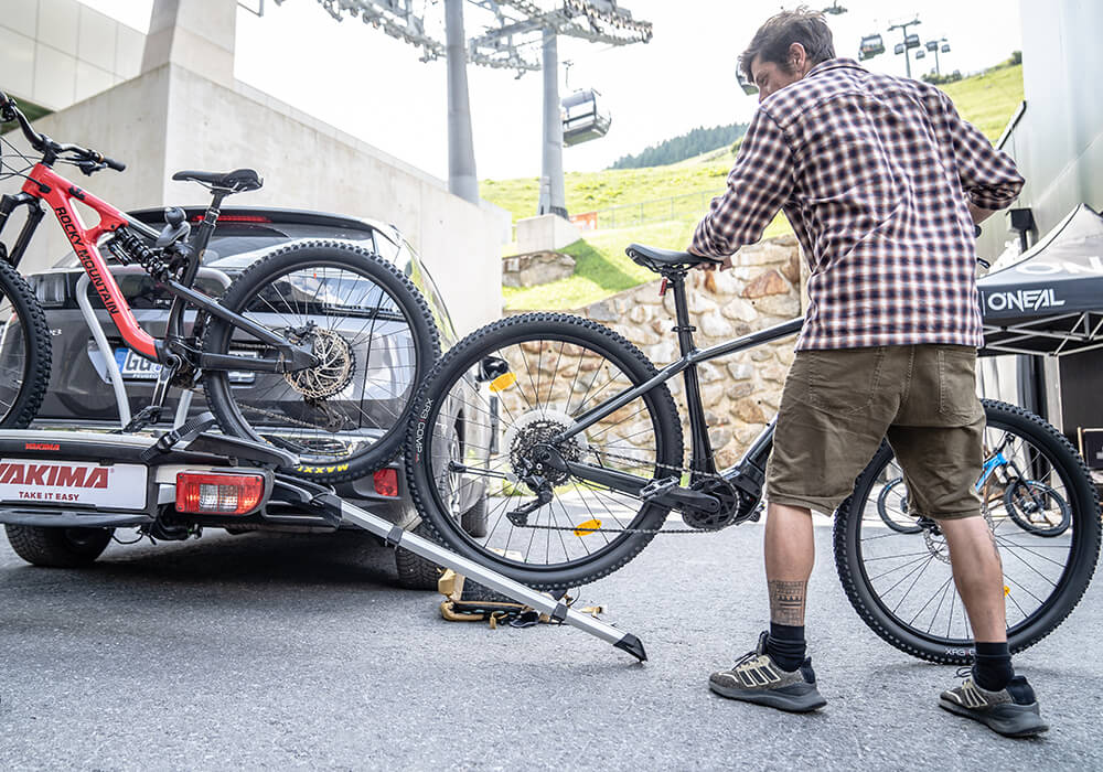 A man uses a loading ramp to load a second mountain bike onto a Yakima tow bar rack