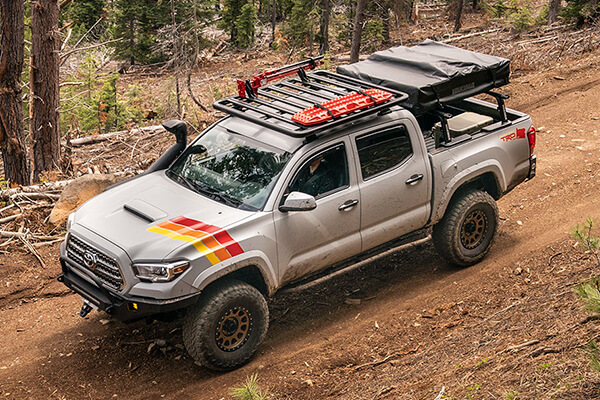 Pick-up truck fitted with a Yakima lock 'n' load platform and a roof tent driving through a forest