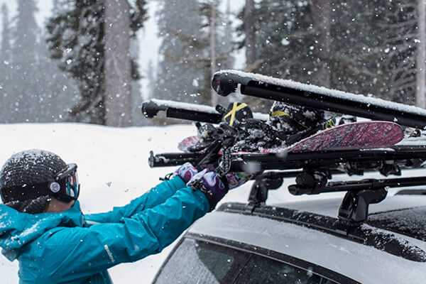A woman takes her snowboard out of her Yakima Fat Cat Evo Snowboard Rack whilst snow falls